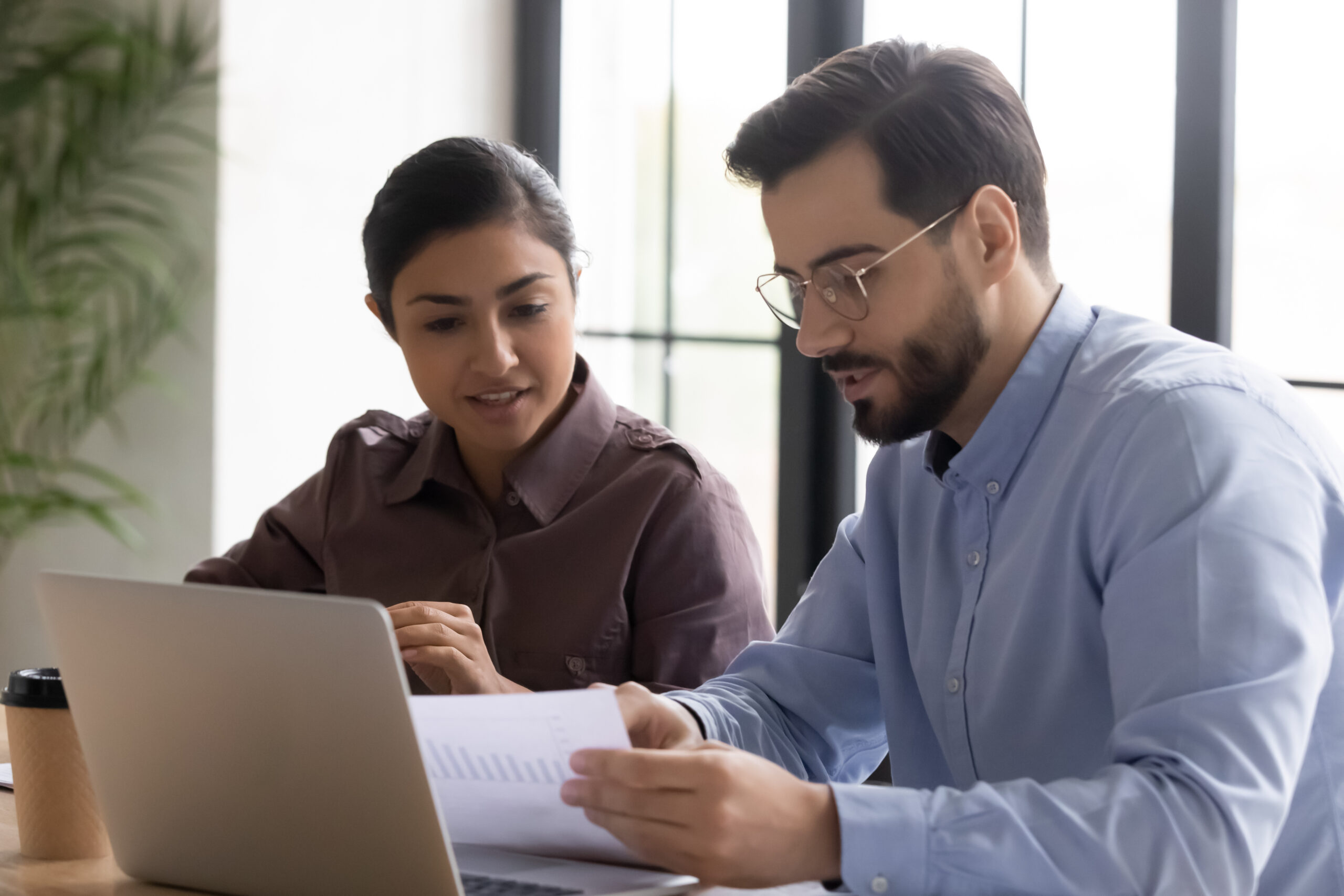 Diverse smiling businessman and businesswoman reading finance report talking looking at document.