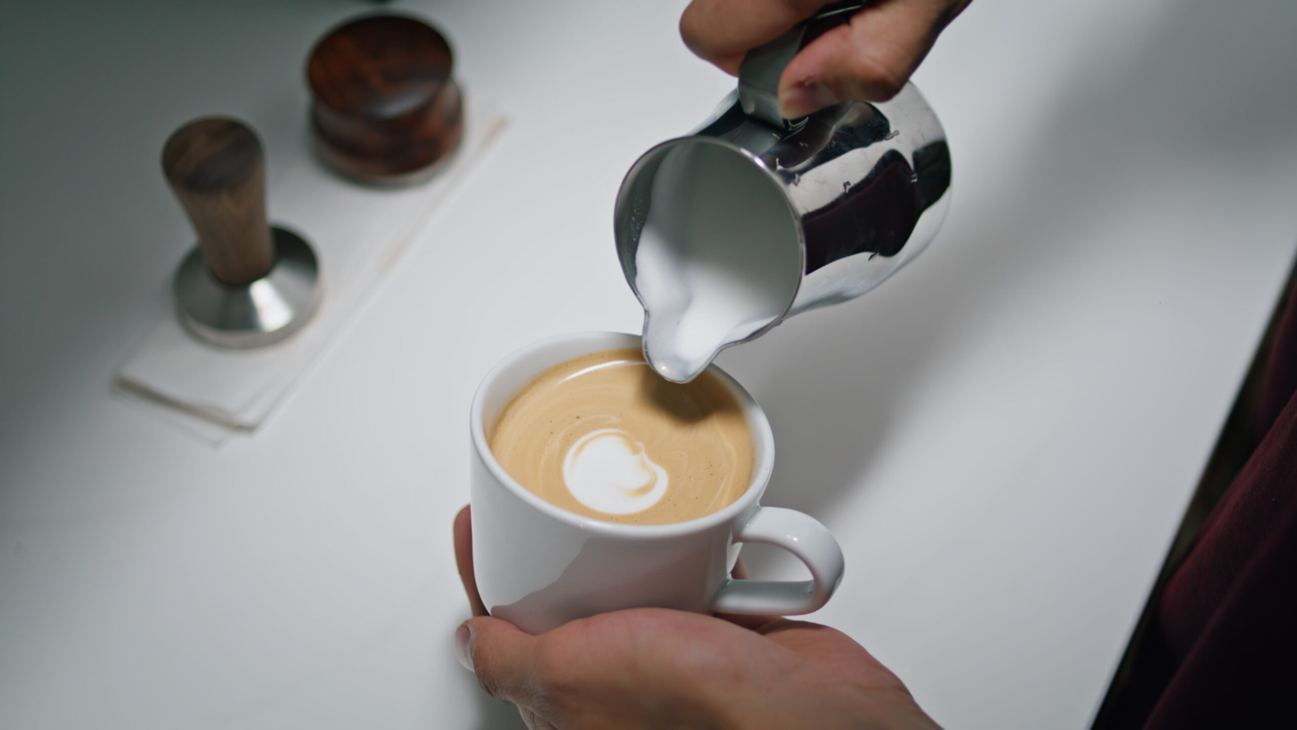 Hands making latte art in coffeeshop close up. Barista pouring milk into coffee.