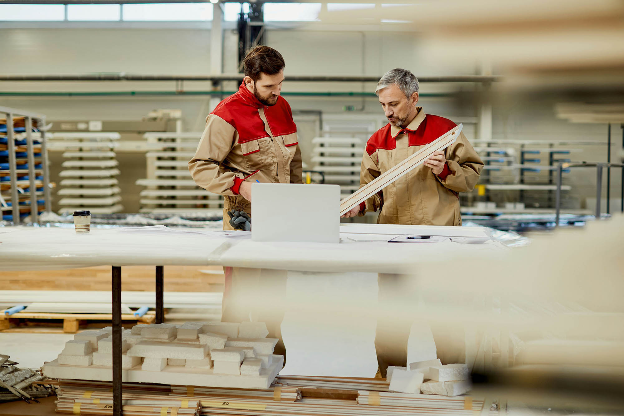 Industrial manufacturing professionals reviewing materials and using laptop for financial consolidation tasks